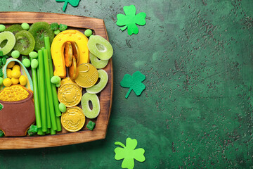 Wooden board with different sweets for St. Patrick's Day celebration on green background, closeup