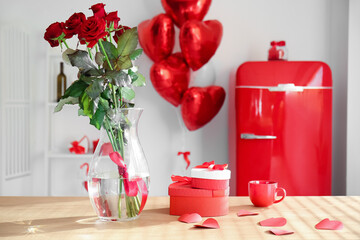 Vase with roses, gift boxes and cup on counter in light kitchen decorated for Valentine's Day celebration