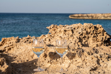 Fototapeta na wymiar Two glasses of cold white dry white wine served on rocks in blue sea bay near Protaras touristic town on Cyprus