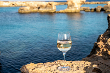 Glass of cold white dry white wine served on rocks in blue sea bay near Protaras touristic town on Cyprus