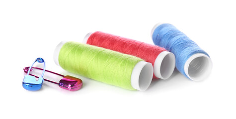 Multicolored thread spools and safety pins on white background