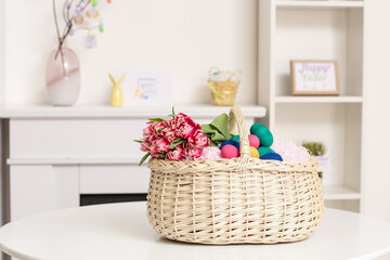 Fototapeta na wymiar Wicker basket with Easter eggs and flowers on table in room