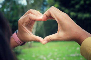 Hands of the person in the shape of heart. Woman making and showing love valentine symbol with hand gesture on blurry garden view background.