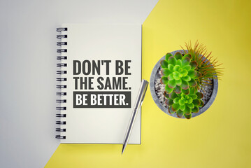 Inspirational motivational quote - Don't be the same. Be better. Personal growth, self improvement concept with text on notebook with pen, green plant on pot on soft white and yellow desk background.