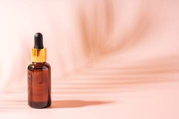 Dark glass bottle with pipette against pink background.