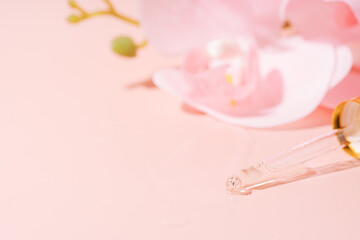 Orchid and pipette filled with liquid on pink background.
