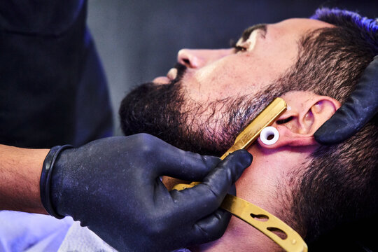 barbero cortando cuidosamente la barba de un joven cliente con una lujosa cuchilla
