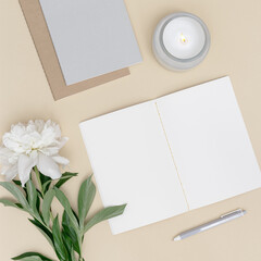 Flat lay, top view office table desk. Workspace with blank copybook, pen, white peony flower with green leaf and fragrant candle as aromatherapy