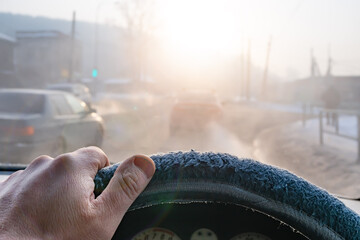 view of the driver hand on the steering wheel of a car moving in traffic with poor visibility on the road