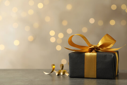 Beautifully wrapped gift box on grey table against blurred festive lights, space for text