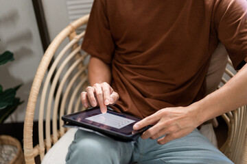 Technology Concept The male with his casual T-shirt and jeans sitting comfortably on the wooden chair and doing touchscreen for checking the web browser on the iPad