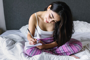 latin young girl writing on notebook on bed at home in Mexico Latin America
