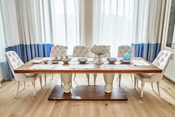 Luxury vintage dining table of walnut solid and veneer wood with festive setting and armchairs near window in spacious room