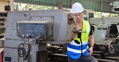 Technician engineer or worker in protective uniform standing and using computer while controlling operation or checking industry machine process with hardhat  at heavy industry manufacturing factory