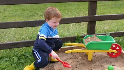 Red headed Child playing with toys in Sand Pit