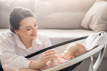 Mom holds little infant daughter by hand in automatic cradle for sleeping, sun light. Concept...
