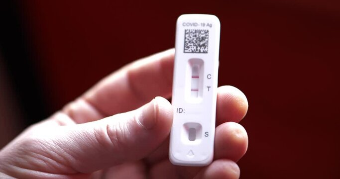 Covid 19 positive antigen test with two red lines control and test in white Caucasian male man hands and fingers as camera pans around slowly as he fidgets with it slightly.