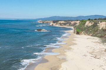Aerial view of empty sandy beach, rocky outcrops, sandstone cliffs, rocky headlands and Pacific ocean on sunny winter day near Half Moon Bay in California