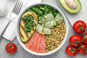 Delicious lentil bowl with salmon, avocado and cucumber on grey table, flat lay