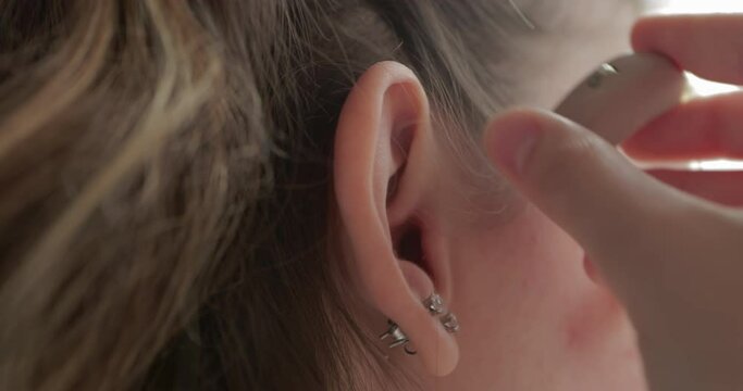 Girl with hearing problems uses a hearing aid after visiting an otolaryngologist. Technology helps people with disabilities in their daily lives. Young deaf woman adjusting hearing aid to environment.