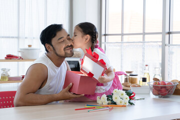 Little mixed race daughter kissing young Asian dad on cheek while giving and opening gift box...
