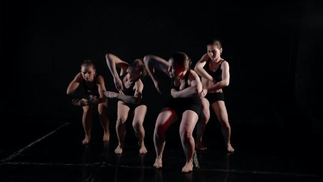 four ballerinas are performing contemporary choreography in dark studio