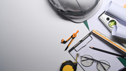 Top view glasses, blueprints, tape measure and hard hat on white table.
