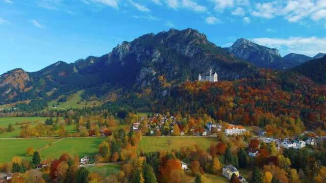 View of drone punching in while slowly flying over village houses towards castle on hill over scenic autumn field in the afternoon near the Neuschwanstein Castle in Germany, Europe, wide view