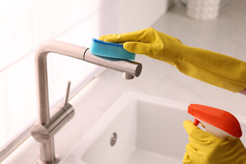 Woman cleaning faucet with sponge and detergent in kitchen, closeup