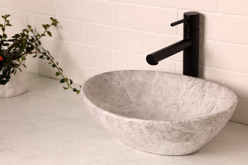 Stone vessel sink with faucet on white marble countertop