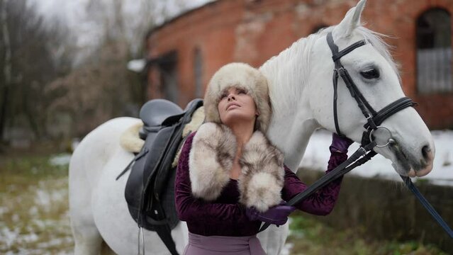 female rider and her white steed in horse yard in winter windy day