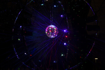 Mirrored Disco Ball and bright beams at the night party. Party attribute reflects Lazer lights. Abstract background with defocused rays. Night club atmosphere. Installation at Vilnius light festival