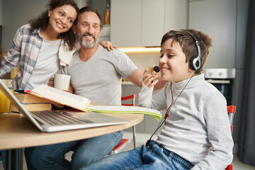 Boy in headset with open book stuying before laptop