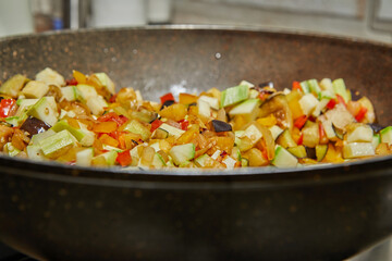 Dish with eggplant, zucchini and bell peppers in frying pan close-up over low heat