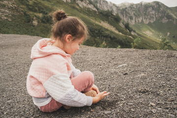 The child sits in the mountains and enjoys the views. A baby in a hoodie and jeans sits on the ground. Traveling with your child in the mountains