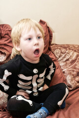A child in a skeleton costume sits on the couch and coughs or yawns - 484322448