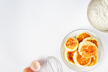 cheesecakes from cottage cheese, bowl with flour, eggshell, whisk for beating on a white background with copy space