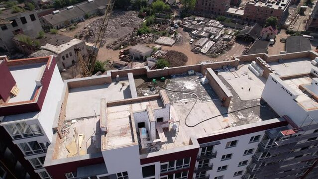Man builder using troweling machine while screeding floor on the roof of residential building. Another man leveling surface with straight edge while screeding floor outdoors in new building.