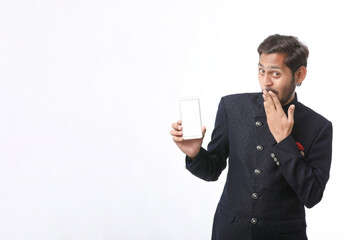 Young indian man in tradition wear and showing smartphone screen on white background.
