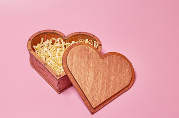 Wooden gift box in the shape of a heart with paper filling with an open lid.