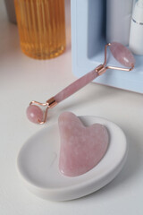 Rose quartz gua sha tool, natural face roller and cosmetic products on white table
