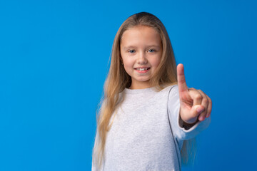 Cheerful teenage girl pointing finger at camera on blue background