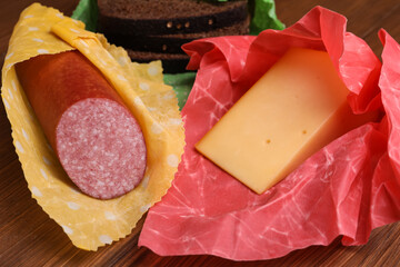 Different products in beeswax food wraps on wooden table, closeup