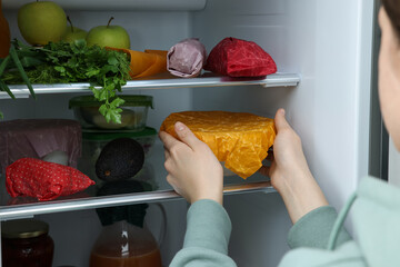 Woman taking bowl covered with beeswax food wrap from refrigerator, closeup
