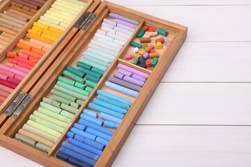 Set of soft pastels in box on white wooden table, space for text. Drawing material