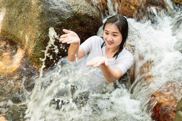 Asian woman hanging out at a waterfall. She wants to have fun on vacation. The waterfall is very cold because it is natural water.
