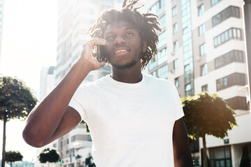 Handsome hipster model.Unshaven African man dressed in white summer t-shirt.Fashion male with dreadlocks hairstyle. Posing in the street.Using has smartphone. Talking with friends at cellphone