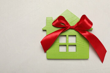 Wooden house model with red bow on white table, top view and space for text. Housewarming party