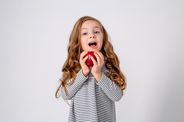 cute little girl with curls in a striped dress is holding a big red apple in her hands. blue background. useful products for children. healthy snack. space for text. High quality photo