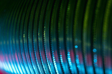 Ridged texture. Color light background. Embossed steel gear wheels. Defocused neon green red blue glow reflection on dark curved corrugated abstract overlay.